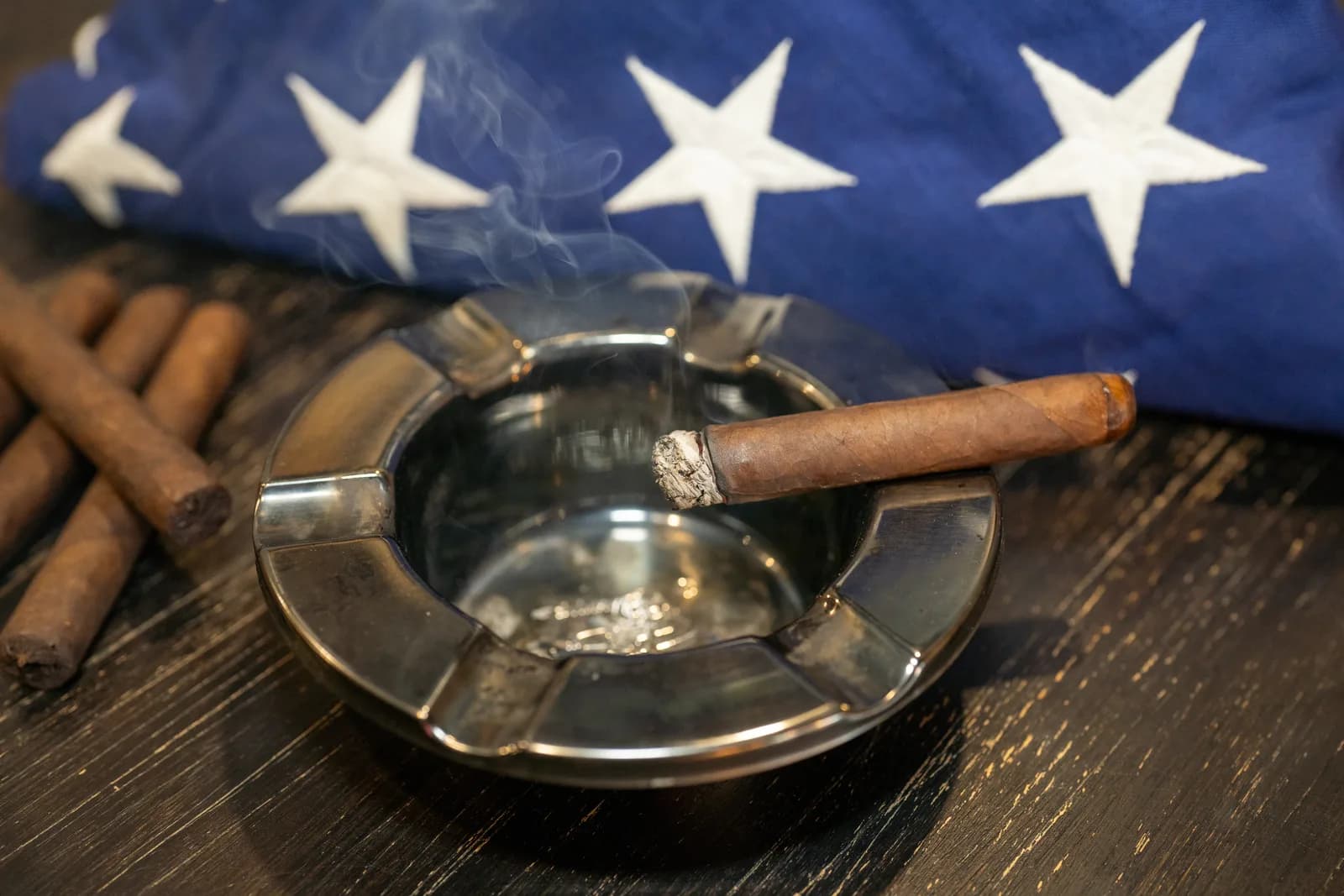 A lit Blue Collar Tobacco cigar resting on a steel ashtray in front of a folded American flag