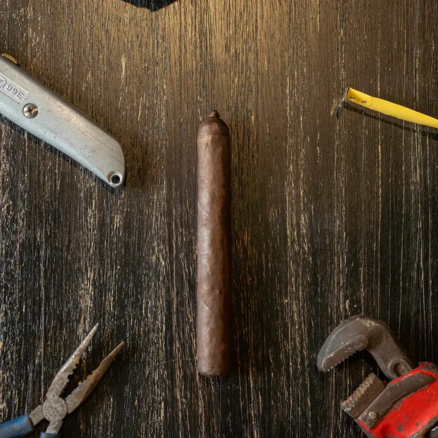 A Blue Collar Tobacco cigar on a dark workbench surrounded by hand tools